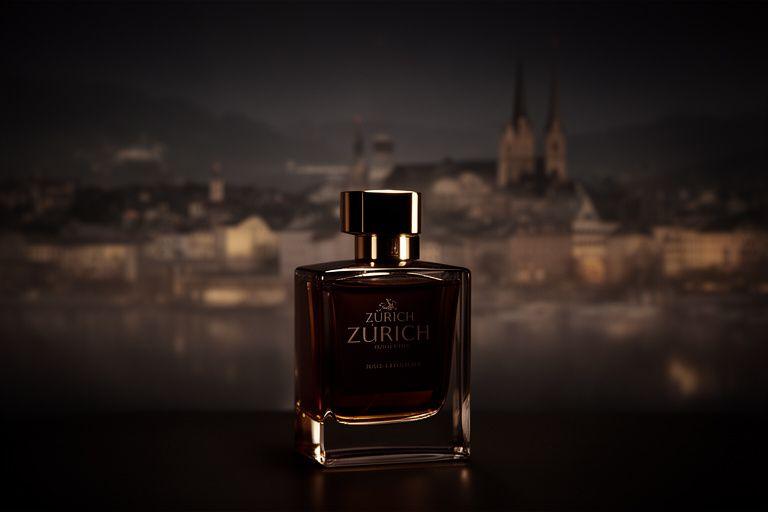 Dunkles Flakon-Stillleben mit warmem Licht und Zürcher Stadtsilhouette im Hintergrund